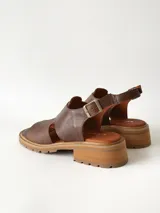 Sandalias de cuero color chocolate con suela track y taco bajo cuadrado. Poseen capellada cerrada con aberturas laterales y tira ajustable en el talón con hebilla metálica.