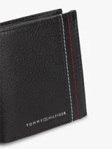 Billetera plegable de cuero granulado color negro, marca Tommy Hilfiger, con costuras decorativas tricolores y logo metálico frontal.