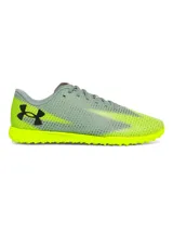 Championes de fútbol Under Armour Shadow Select 3 Turf, diseñados para césped artificial. Presentan un empeine sintético suave y resistente en color gris con detalles en amarillo neón, incluyendo el logo de la marca en negro. Cuentan con suela de goma con tacos multidireccionales para un agarre óptimo.