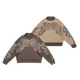 Sweater tejido reversible de corte boxy fit, con cuello redondo y puños acanalados. Presenta un diseño gráfico abstracto de estilo gótico que recorre el pecho y las mangas. Un lado es de color marrón oscuro con detalles en beige, y el otro lado es de color beige con detalles en marrón oscuro.