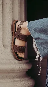 Sandalias planas de cuero color marrón chocolate, con dos tiras anchas en el empeine decoradas con costuras artesanales y tira ajustable con hebilla en el talón.