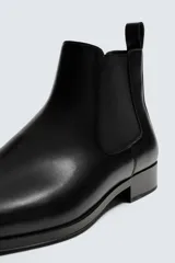 Bota estilo chelsea de cuero color marrón, con paneles elásticos laterales, tirador trasero y horma en punta con suela de tacón bajo.