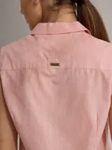 Camisa sin mangas de lino, color blanco, con cuello solapa, cierre frontal con botones y bolsillo pequeño en el pecho. Presenta costuras decorativas a la vista que definen la silueta.
