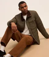 Campera puffer negra con cuello alto, cierre frontal con botones a presión, bolsillos laterales y un bolsillo cargo en el pecho. Presenta un diseño acolchado y forro interior suave.