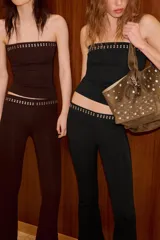 Top tipo bandeau negro de tejido elástico, con escote recto, hombros descubiertos y detalle de tachas metálicas en el borde superior.