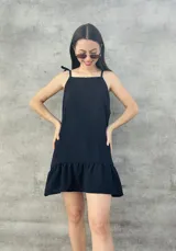 Vestido corto negro con textura de lunares, breteles finos con lazo y falda con volados.