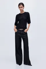 Remera de punto pointelle suave de color negro, con cuello redondo ribeteado acanalado y mangas raglán al codo. Presenta remate acanalado en mangas y bajo.