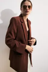 Blazer marrón de cuello solapa con muescas, manga larga y bolsillos de vivo con solapa. Cierre frontal con un botón.
