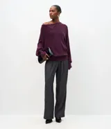 Suéter de tricot color bordó, con textura acanalada, corte recto y caída suelta. Presenta diseño de hombro caído, manga larga, cuello asimétrico con solapa estructurada y detalle de botones decorativos en el hombro.