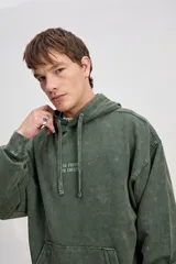 Canguro de algodón con efecto lavado de corte oversize, capucha con cordones ajustables, bolsillo canguro delantero y estampa frontal con texto en el pecho.