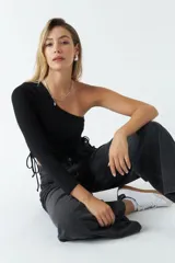 Top asimétrico de una sola manga larga, color negro, con jaretas laterales ajustables que permiten regular el largo de la prenda.