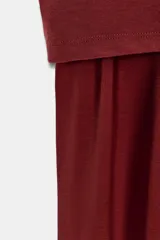 Vestido largo color borgoña, con escote barco y manga caída/sisa. Presenta un drapeado lateral que genera un bajo asimétrico.