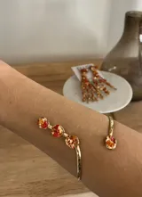 Brazalete abierto de metal dorado con acabado martillado, decorado con cuatro piezas circulares que contienen incrustaciones de piedras en tonos rojizos, naranjas y dorados.