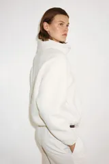 Campera deportiva de sherpa en color blanco, de corte holgado, con cuello elevado, cierre frontal y bolsillos laterales.