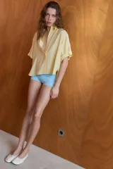 Camisa de corte fluido con cuello solapa y manga corta con dobladillo. Presenta cierre frontal con botones ocultos bajo una tapeta.