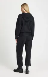 Pantalon tipo jogger de tiro alto, color negro, confeccionado en tejido de punto. Presenta una cinturilla elástica ancha con cordón ajustable y detalle de superposición de encaje en la parte delantera. Cuenta con bolsillos laterales ribeteados, perneras ligeramente holgadas y puños ajustados con elástico.