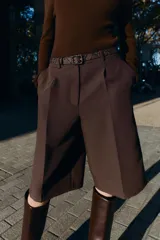 Bermuda larga color marrón oscuro, tiro medio, con pinzas frontales y cinturón de textura animal print plateado.