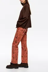 Pantalón de denim de corte recto y tiro alto, con diseño de cinco bolsillos y cierre frontal con botón y cremallera. Presenta un estampado de manchas oscuras sobre base de color terracota.