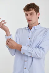 Camisa de vestir blanca de manga larga, con cuello abotonado, bolsillo frontal y botones en tono madera.