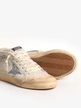 Zapatillas urbanas de caña media, color blanco hueso, con detalles desgastados. Presentan una estrella de glitter plateado en el lateral, cordones blancos y suela de goma color caramelo.