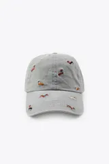 Gorra de sarga confeccionada en algodón, con visera curva y ajuste posterior. Presenta un diseño de color gris con múltiples bordados pequeños de perros salchicha en diversos colores.