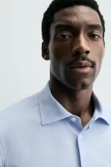 Camisa de manga larga, color celeste con finas rayas verticales blancas, cuello italiano y cierre frontal de botones.