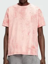 Remera de manga corta, cuello redondo y calce holgado, color rosa pálido con un efecto de teñido o estampado que simula grietas o craquelado en tonos más oscuros de rosa/naranja.