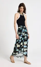 Pollera larga de corte evasé con estampado abstracto en tonos azules, negros y beige. Presenta cintura alta con diseño cruzado, pliegues suaves que aportan movimiento y un acabado con sutil transparencia en el bajo.