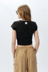 Top corto de manga corta, color negro con efecto desgastado o acid wash, cuello redondo y costuras verticales que definen la silueta.