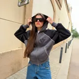 Campera canguro Nude Project con cierre frontal, capucha y bolsillos tipo kadoro. Diseño bicolor con cuerpo gris y mangas negras, con detalles de costuras visibles y logo bordado en el pecho.
