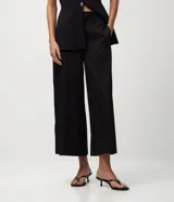 Pantalón pantacourt negro de sastre, con cintura alta, cierre interno discreto y pliegues delanteros sutiles.