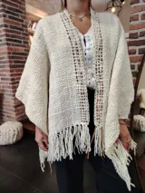 Ruana de lana color crudo, tejida a mano con diseño calado en el frente y flecos en el ruedo.