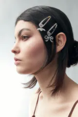 Set de dos clips plateados para el pelo, uno con dije de corazón alado y otro con dije de moño.