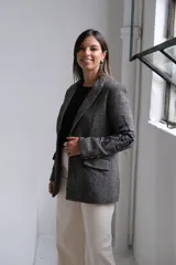 Blazer de corte sastrero en color gris con patrón de rayas diagonales y bordados negros en las mangas y solapas. Presenta cierre frontal con botón, bolsillos con solapa y estructura clásica.