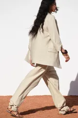 Blazer color beige confeccionada en lino, de corte recto, con cuello solapa, hombreras y mangas 3/4 con trabilla y botón dorado.