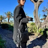 Bolso tipo morral y bandolera de eco-cuero negro, con cierre superior, bolsillos frontales con cierre y correa ajustable para el hombro.