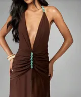Vestido largo color chocolate con escote en V profundo, tirantes finos decorados con piedras turquesas y fruncido en la cintura con una hilera de piedras turquesas. La falda es fluida y semitransparente.