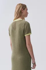 Vestido largo verde de tejido de punto calado, con escote redondo y mangas cortas. Tiene tajos laterales y ribetes en color amarillo.