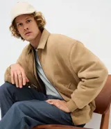 Campera bomber de gamuza sintética color tostado, con cuello camisero, cierre frontal metálico, bolsillos frontales con solapa y rib elástico en puños y ruedo.