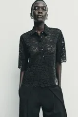 Camisa de encaje negro con cuello solapa, manga corta y cierre frontal con botones.