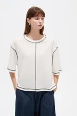 Remera de algodón color crudo, con cuello redondo a la base, mangas 3/4 holgadas y costuras con pespuntes en tono contrastante.