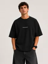 Remera de algodón premium color negro, con corte boxy, cuello redondo y mangas cortas amplias que llegan hasta el codo. Cuenta con un pequeño texto estampado en el centro del pecho.