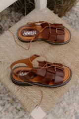 Sandalia de cuero vacuno color marrón, con diseño moderno de tiras anchas entrecruzadas, pasadores con cordón ajustable en el empeine y suela track robusta.