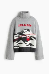Sweater de punto gris con cuello alto acanalado, diseño jacquard frontal con paisaje de montaña y teleférico en colores blanco, negro y rojo, y hombros caídos.