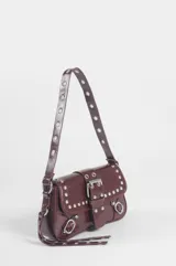 Cartera de hombro de cuero sintético color bordó, con solapa frontal decorada con tachas plateadas, hebillas y herrajes metálicos. Cuenta con un asa larga ajustable adornada con ojales metálicos.