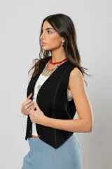 Chaleco negro con escote en V, sin mangas y cierre frontal con botones. Presenta pespuntes en color crudo en la parte delantera y logo bordado en la espalda.