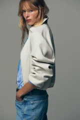 Chaqueta bomber negra con cuello solapa, manga larga abullonada y puños elásticos. Presenta falsos bolsillos de doble vivo en la parte delantera y cierre frontal con cremallera.