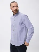 Camisa de manga larga con diseño de rayas finas verticales en azul y blanco, cuello clásico con botones y cierre frontal. Presenta un pequeño bordado en la pechera y puños abotonados.