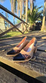 Zapato de tacón ancho de punta fina con combinación de texturas, puntera de charol negro, detalle animal print y cuerpo en tono tostado. Cuenta con hebilla lateral ajustable.