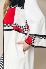 Túnica larga color marfil con vivos negros de satén, bolsillos laterales y diseño geométrico con bloques de color rojo y negro.